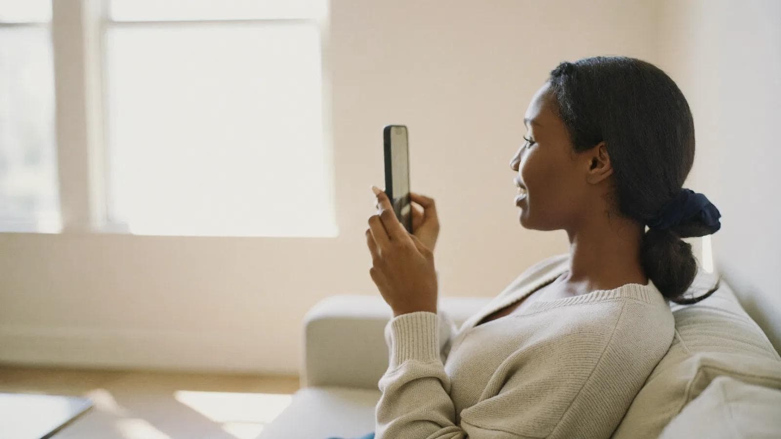 Kobieta na jasnej sofie zadaje pytanie telefonowi i spokojnie czeka na odpowiedź